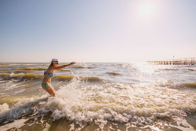 Cheerful mid adult woman playing at beach against clear sky