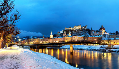 Illuminated bridge over river against blue sky during winter