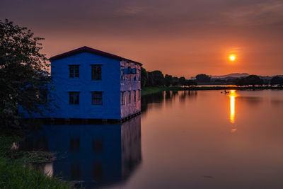 Building by lake against sky during sunset