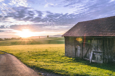 Old wooden house on field against sky during sunset