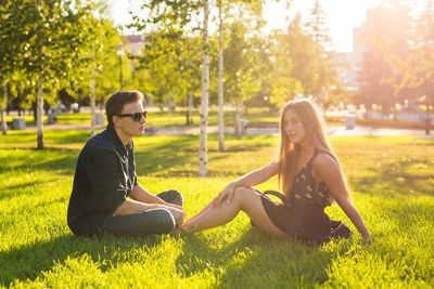 Young couple sitting on grass against trees