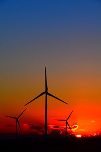 Silhouette wind turbines on field against sky during sunset