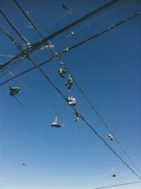 Low angle view of shoes hanging on cables against clear blue sky