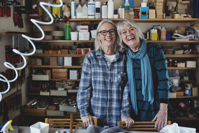 Portrait of cheerful colleagues standing against shelf at workshop