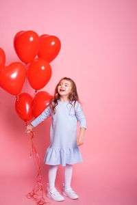 Beautiful child girl with red heart romantic balloons on pink background. concept of valentine day