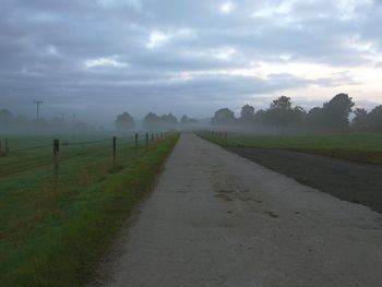 Road passing through field against cloudy sky