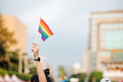 Cropped hand of woman holding rainbow flag against buildings