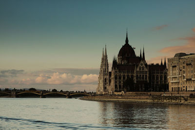 Bridge over river by buildings against sky during sunset