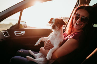 Portrait of smiling woman sitting in car with dog during sunset