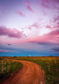 Dirt road amidst field against sky