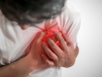 Midsection of man holding aching chest standing against white background