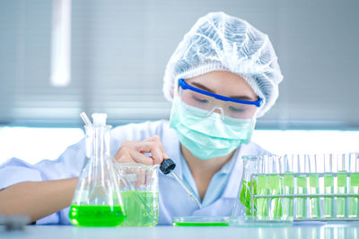Scientist putting green liquid into petri dish
