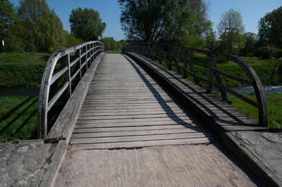 Empty footbridge amidst trees against sky