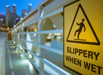 Close-up of slippery road sign on railing during sunset