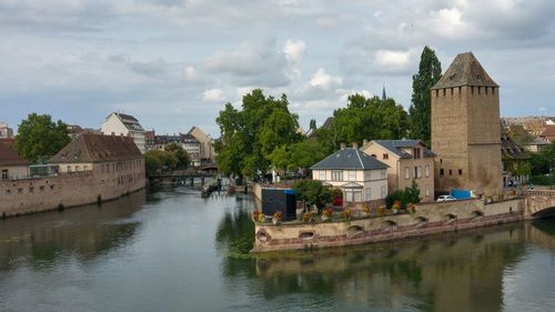 Buildings by river against cloudy sky