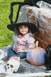 Portrait of smiling girl wearing hat while sitting by pumpkin during halloween