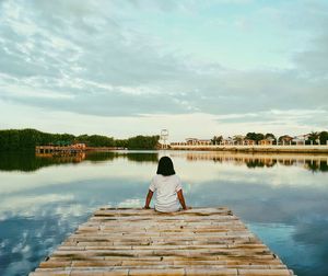 Rear view of woman sitting on pier at lake