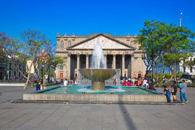 People in front of building against clear blue sky