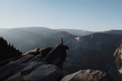 Rear view of man standing on rock against sky