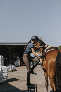 Side view of woman getting on horse at paddock