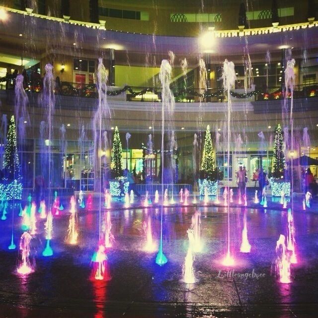 illuminated, water, reflection, night, waterfront, fountain, motion, blurred motion, glass - material, building exterior, transparent, incidental people, celebration, built structure, multi colored, city, spraying, long exposure, architecture, arts culture and entertainment