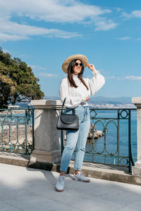 Portrait of young woman standing by railing against sky