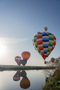 Hot air balloons flying over lake against sky