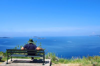 Rear view of man sitting on bench at observation point against sea