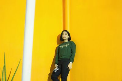 Portrait of woman standing against yellow wall