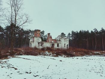 Bare trees on snow covered field against sky