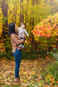 Mother carrying daughter while standing by tree during autumn