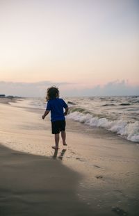 Rear view of boy on beach against sky during sunset