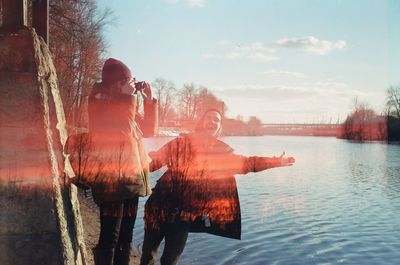 Double exposure of people standing by river and silhouette trees against sky