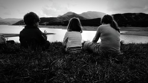 Rear view of siblings sitting at lakeshore