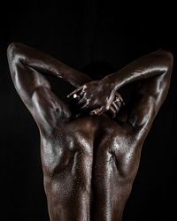 Rear view of shirtless muscular man with sweat standing against black background