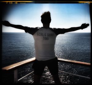 Rear view of man standing by railing against sea