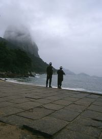 Men standing on mountain by sea against sky