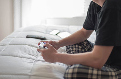 Low section of man playing video game on bed at home