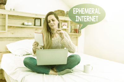 Young woman using phone while sitting on laptop