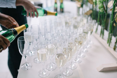 Cropped hands pouring drink in champagne flutes on table