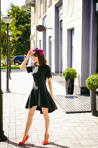 Beautiful young woman in black dress standing on sidewalk in city