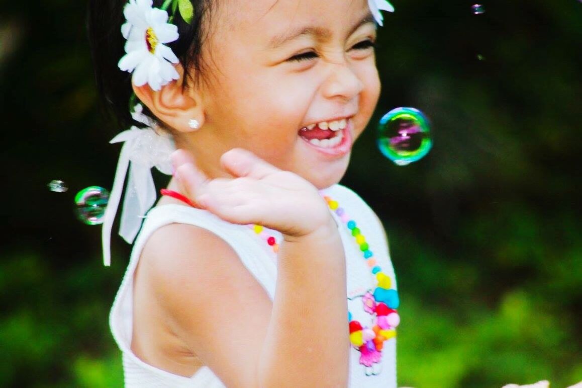 CLOSE-UP OF SMILING GIRL HOLDING BUBBLES AT PARK