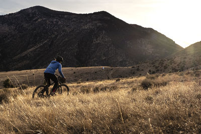 Young woman mountain biking uphill during sunset in mountains