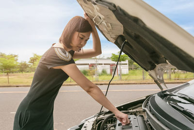 Side view of woman checking car engine on road