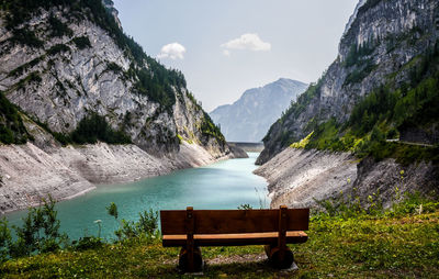 Empty bench in front of river amidst rocky mountains