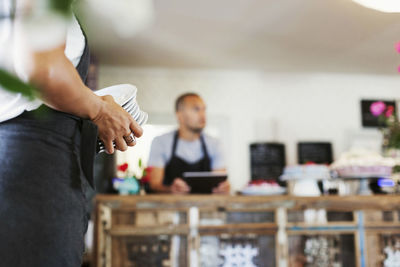 Woman holding stack of plates while coworker standing at cafe counter