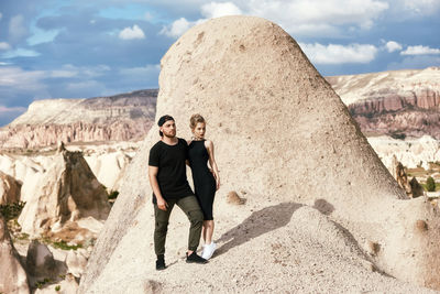 Portrait of young man standing on rock against sky