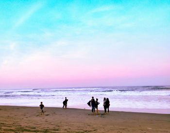People at beach against sky during sunset