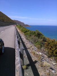 Scenic view of road by sea against clear blue sky