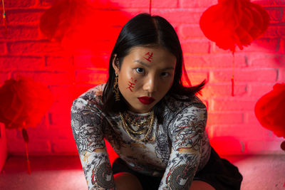 Portrait of young woman sitting against red wall